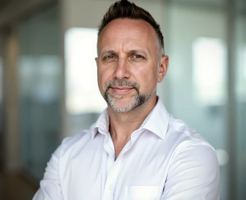 Matt Barnes, coach at Realise Training Group, wearing a white dress shirt and standing confidently in a modern office.